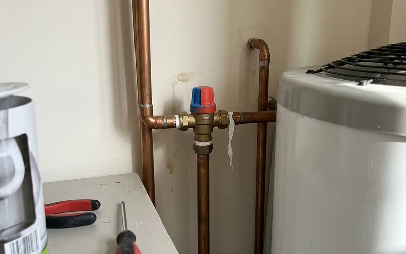 Close-up of a coloured-cap tempering valve on hot water pipework